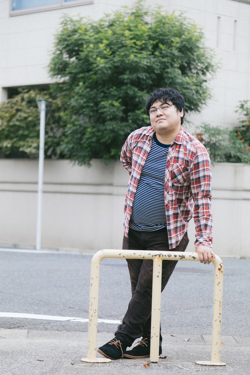 駐車場でチェックシャツを着た男性が何かを見つめている様子［モデル：段田隼人］