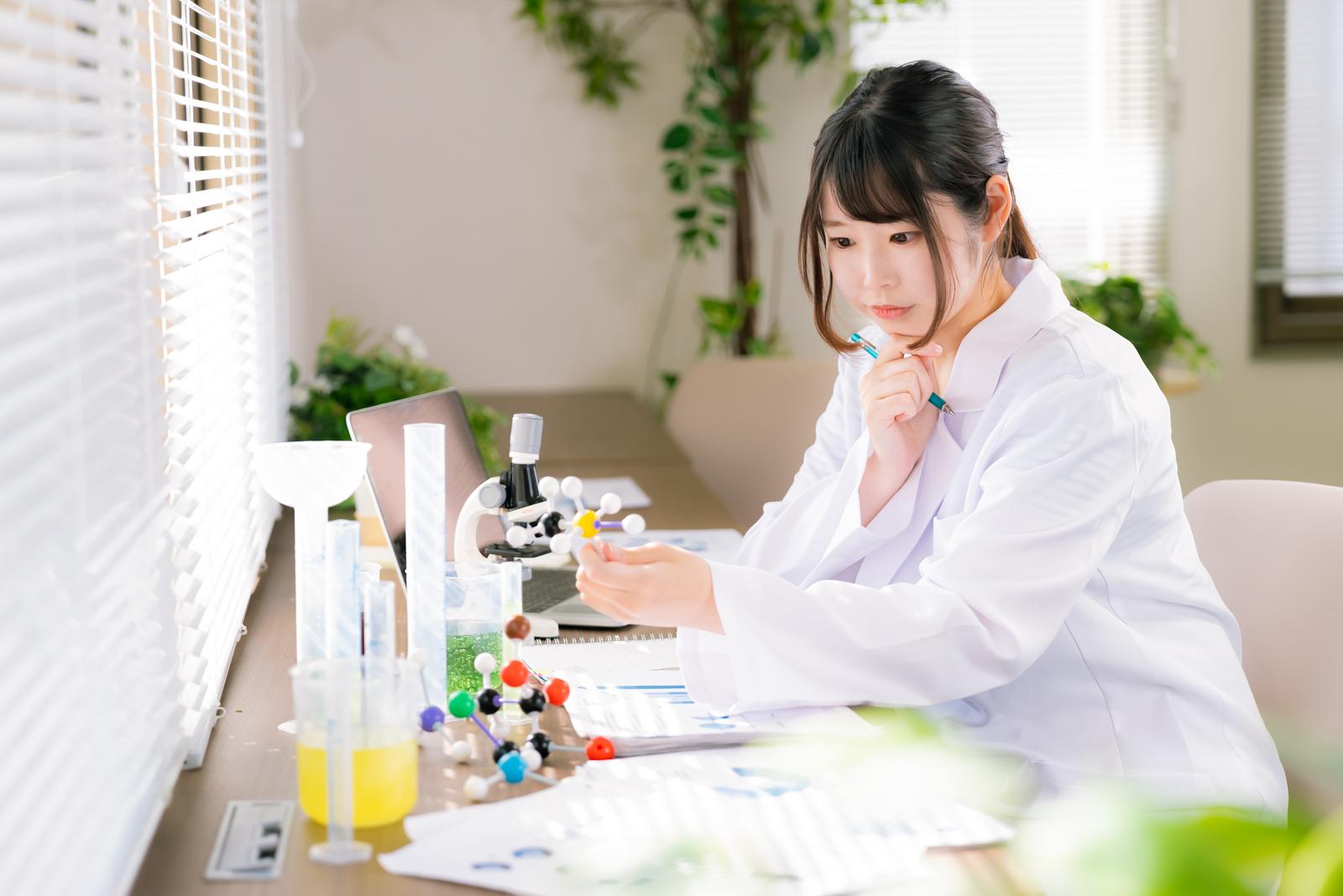 白衣を着た女性が研究室で顕微鏡を操作して実験を行っている［モデル：モデルリリース］