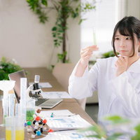 試験管を手に取り中身を観察する白衣を着た女性研究者の写真