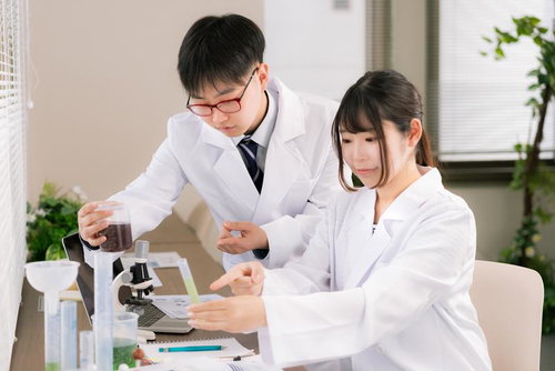 研究室で実験器具を使い白衣を着た男女が共同研究