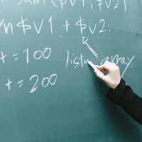 黒板に書かれたプログラミングコードと講師の手の写真