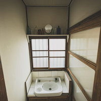古民家の手洗い場の白い陶器洗面台と蛇口、木枠の窓の写真