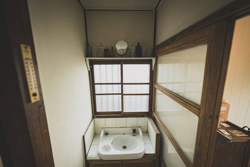 古民家の手洗い場の白い陶器洗面台と蛇口、木枠の窓