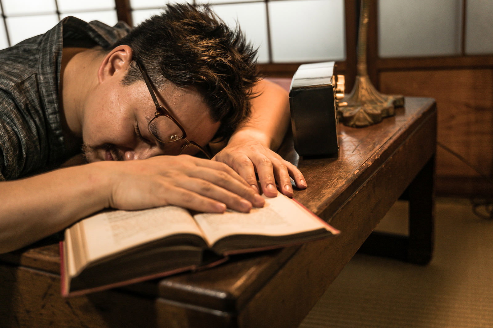 書斎の木製机で本を読みながら寝落ちしている男性［モデル：Max_Ezaki］