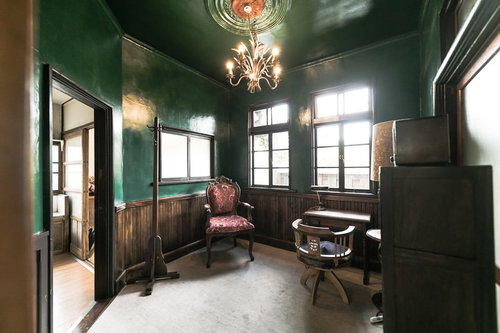 深緑の壁に囲まれた古民家の洋室でアンティーク家具が映える空間