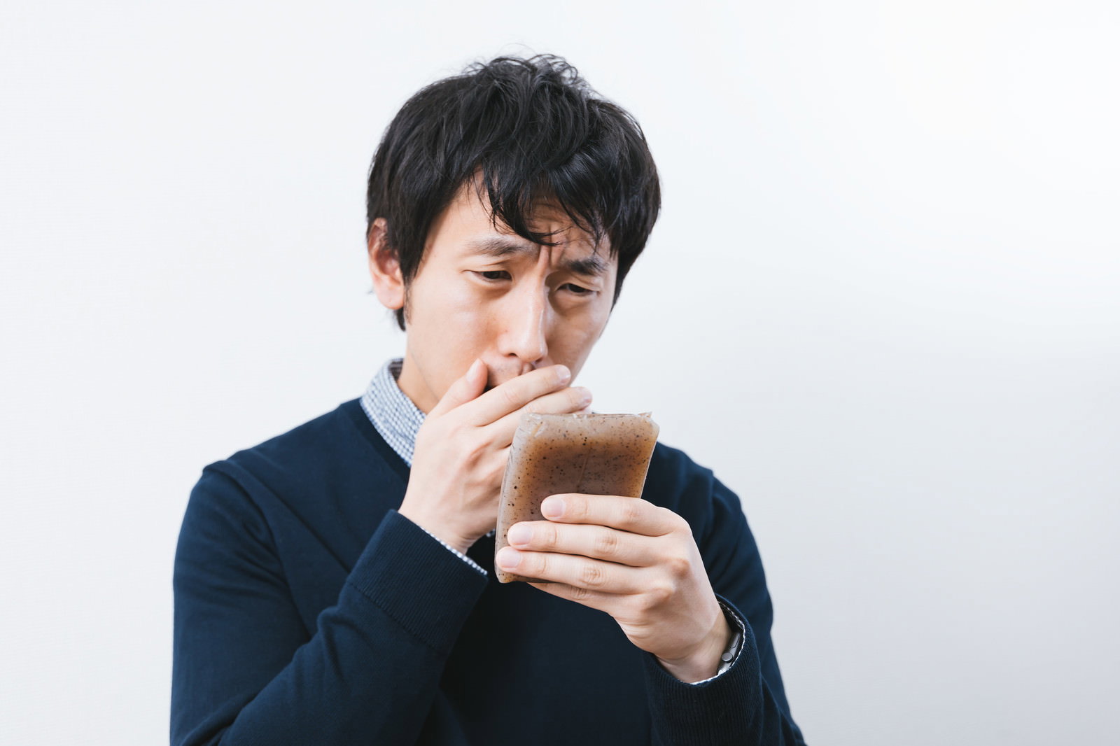 こんにゃくの匂いを嗅いで困惑した顔の紺ニット男性［モデル：大川竜弥］