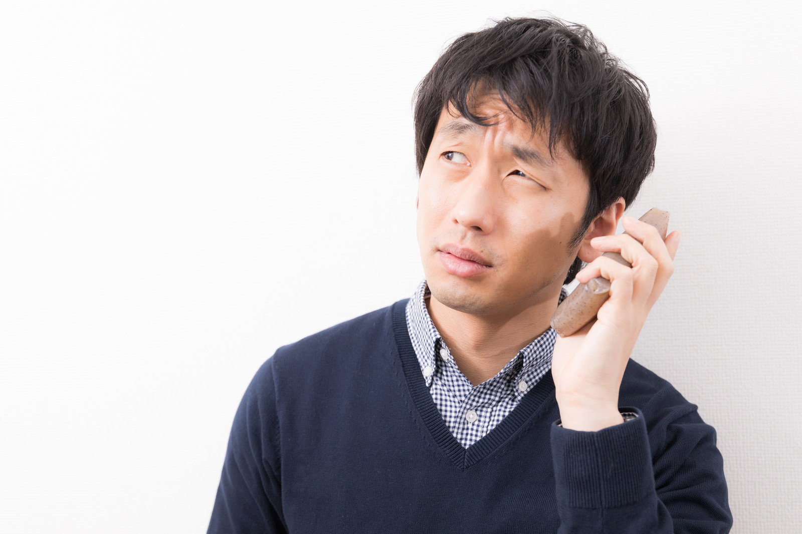 こんにゃくを耳に当てて困り顔の男性［モデル：大川竜弥］