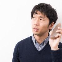 こんにゃくを電話のように耳に当てて困る男性の写真