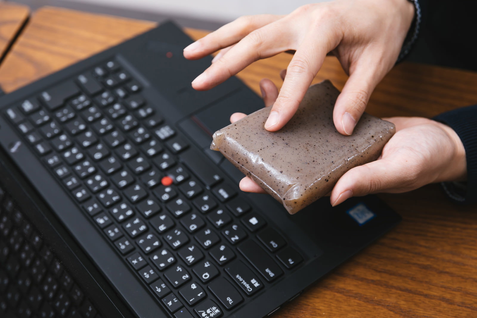 ノートパソコンのキーボード前で、こんにゃくをスマートフォンに見立ててピンチアウト操作する男性の手元［モデル：大川竜弥］