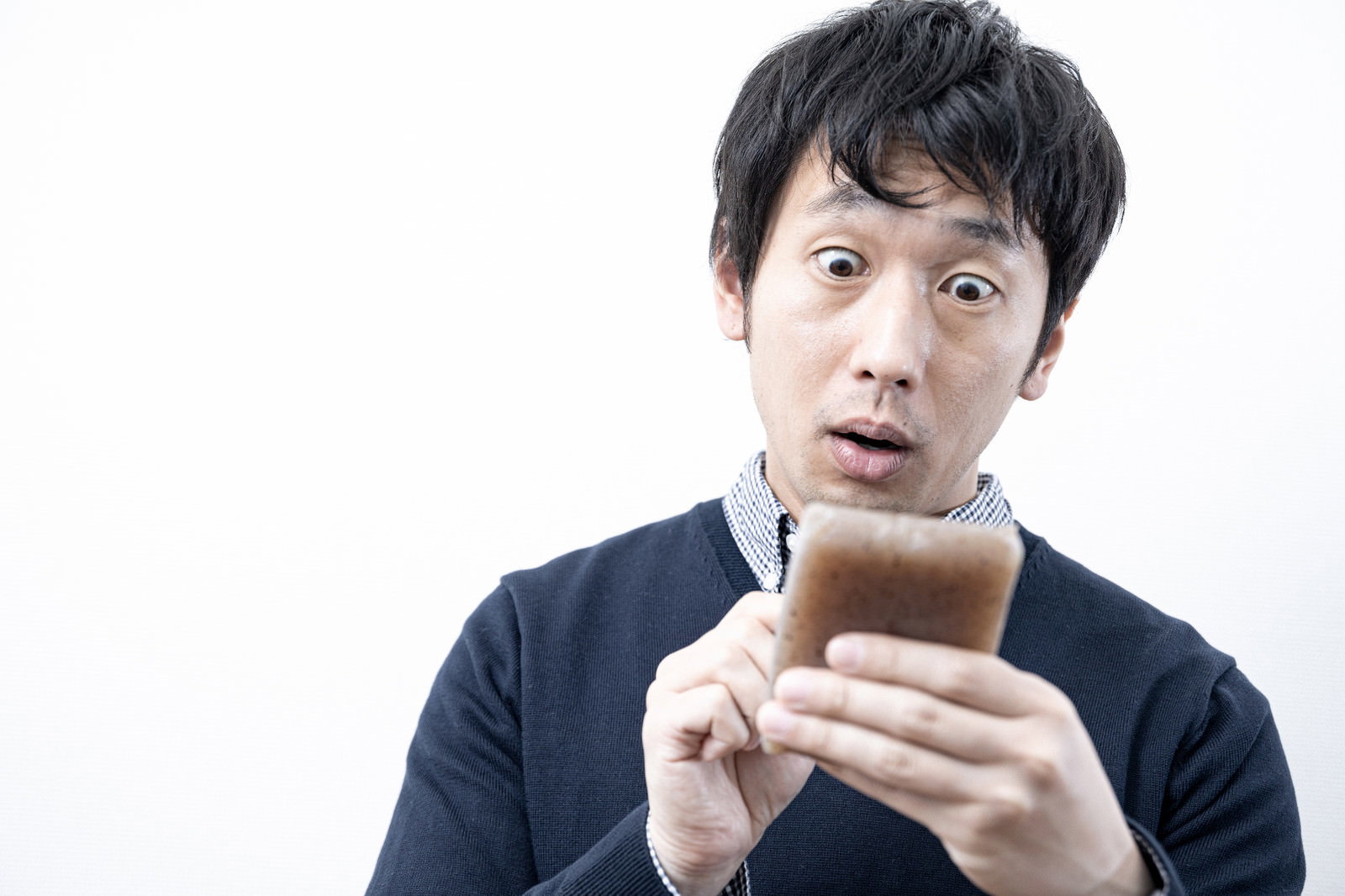 スマートフォンを持って驚いた表情を見せる黒髪の男性［モデル：大川竜弥］