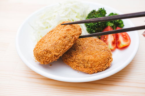 箸でつまんだコロッケを食べる揚げたての一品