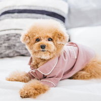 白いベッドでくつろぐピンクパジャマ姿のトイプードルの写真