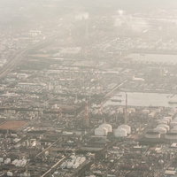 霞む夕暮れの工業地帯、白いタンクと住宅地が薄靄に包まれた航空の写真