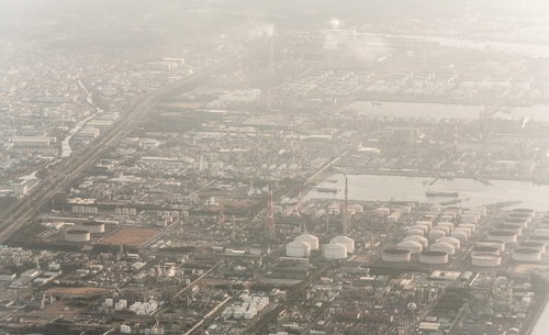 霞む夕暮れの工業地帯、白いタンクと住宅地が薄靄に包まれた航空