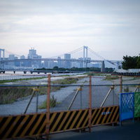 工事用ガードフェンス越しに見えるレインボーブリッジと海岸の写真