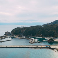 神津島の多幸湾上空から見た漁港と漁船、緑の山々に囲まれた景観の写真