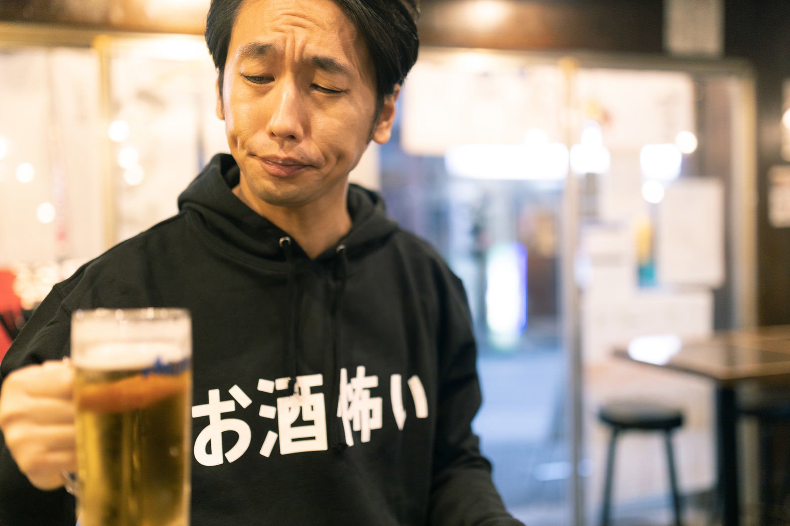 ビールを片手に困惑した表情を見せる黒いパーカーの男性［モデル：大川竜弥］