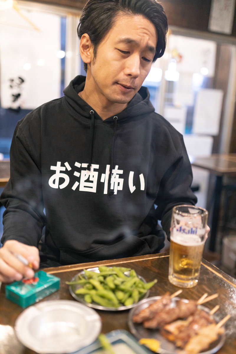 居酒屋のテーブルで疲れた表情を見せる黒いシャツの男性［モデル：大川竜弥］