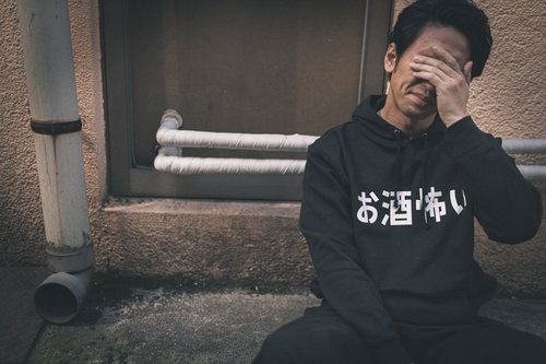 路上の階段で頭を抱える二日酔いの男性、マジでお酒怖い