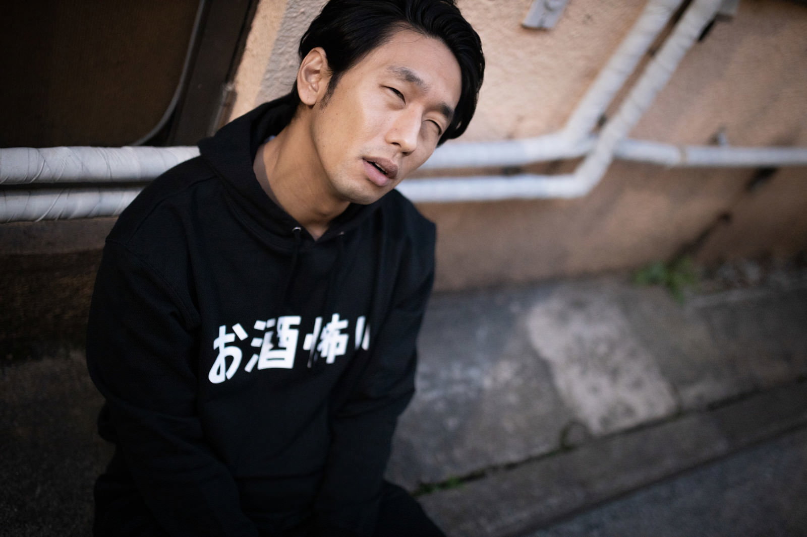 飲みすぎて路上に座り込み呆然とした表情で頭を抱える黒いパーカーの男性［モデル：大川竜弥］