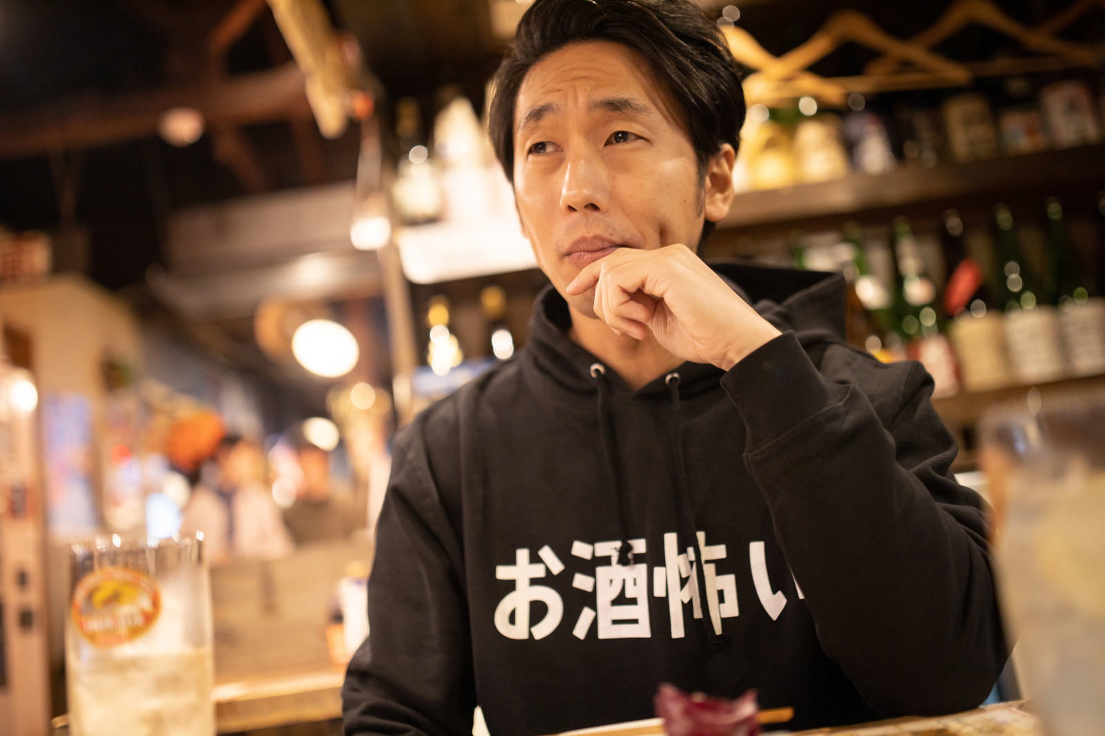 居酒屋で頬に手を当て困惑した表情の男性とハイボール