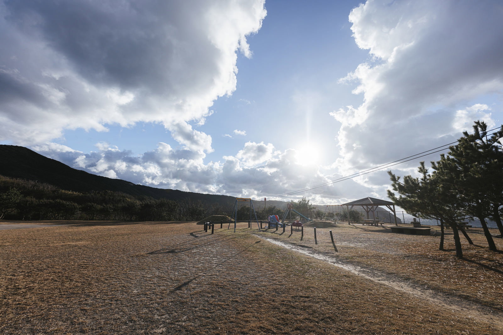 青空に立体的な雲が浮かぶ公園の広場風景、ベンチと山々が見える