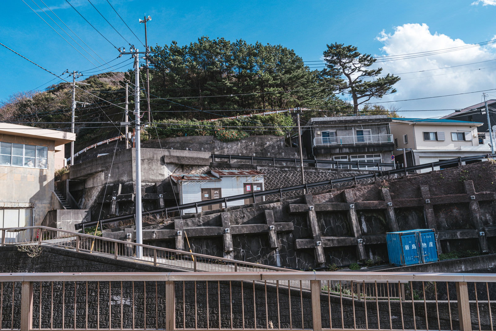 川を隔てて見える住宅街の坂道、青空と雲が広がる神津島の風景