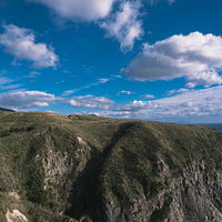 神津島灯台前から眺める森に覆われた崖と青空の写真