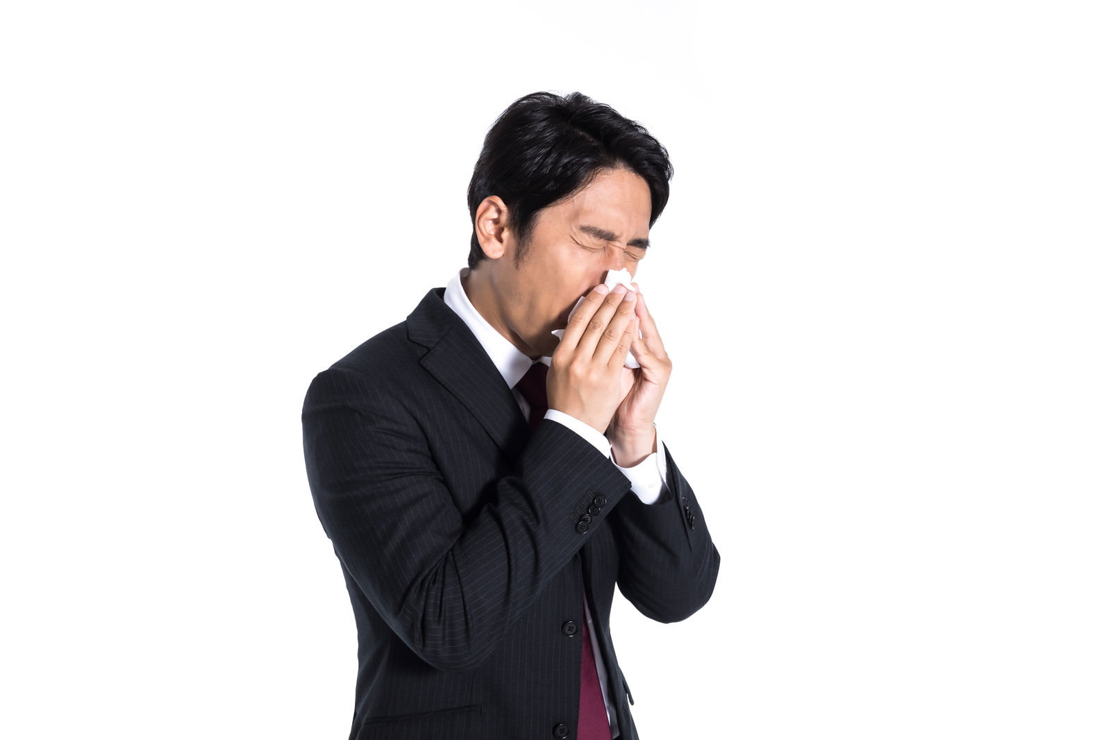 白いティッシュで鼻をかんでいる黒いスーツ姿の男性［モデル：大川竜弥］