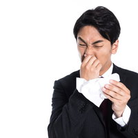 ティッシュで鼻をかむ都会人の男性サラリーマンの写真