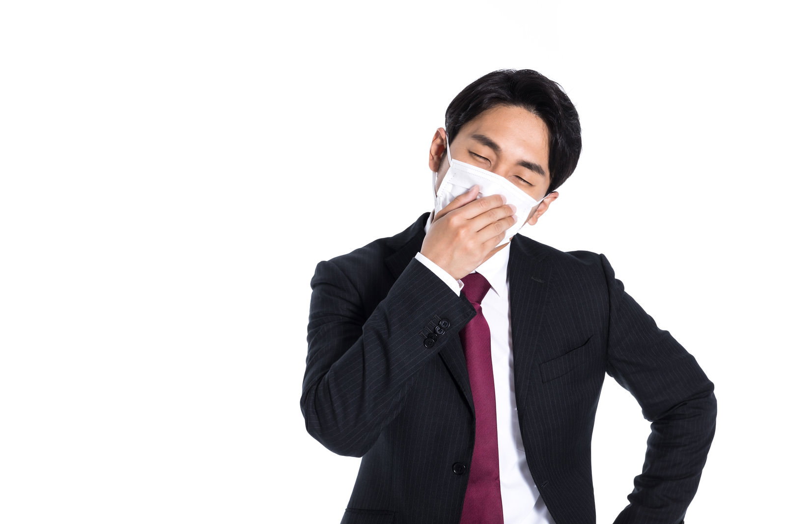 白いマスクを着用し手を額に当てる濃いスーツ姿の会社員男性［モデル：大川竜弥］