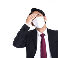 マスクをして頭痛に苦しむサボり社員、体調不良で仕事ができないの写真