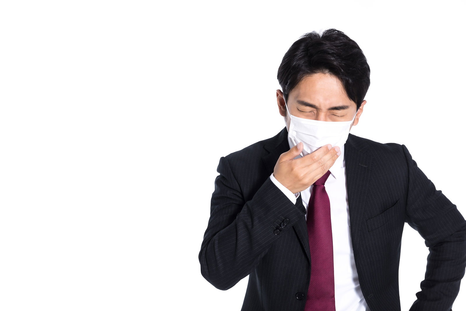 黒いスーツを着てマスクをつけた会社員が手で口元を押さえて咳き込んでいる［モデル：大川竜弥］