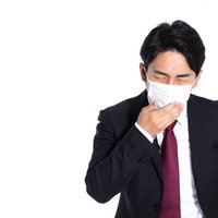 マスク越しに咳き込む会社員男性の感染症対策の写真