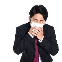 マスクを両手で押さえて咳を我慢する会社員男性の写真
