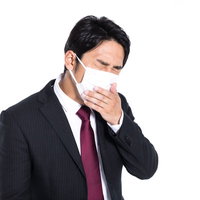 マスク着用しながら咳が止まらない会社員男性の写真