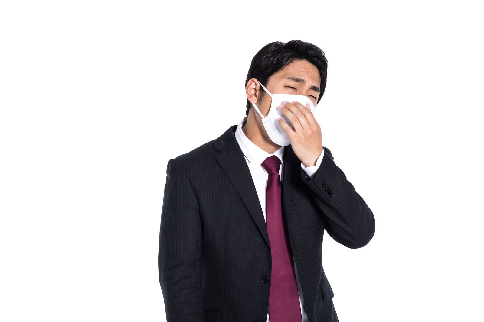 白いマスクを着用し口元に手を当てて口臭を気にするスーツ姿の会社員男性［モデル：大川竜弥］
