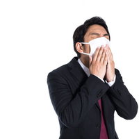 マスクを着用してもくしゃみが止まらない会社員の写真