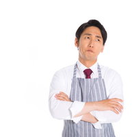 白いエプロンを着用して腕組みで考え込む営業マンの写真