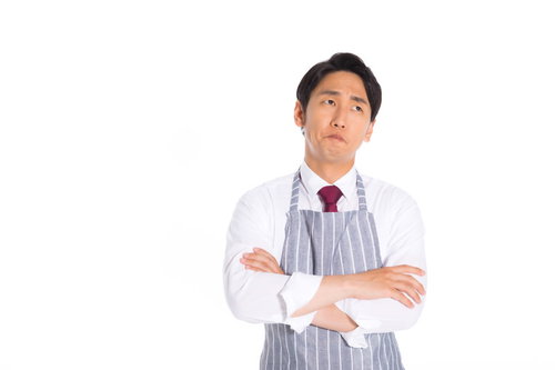 白いエプロンを着用して腕組みで考え込む営業マン