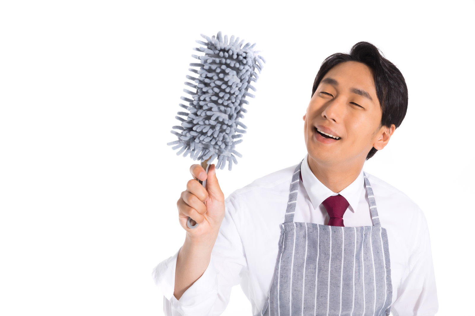 白いエプロンを着た男性販売員がモップを持って笑顔でポーズしている［モデル：大川竜弥］
