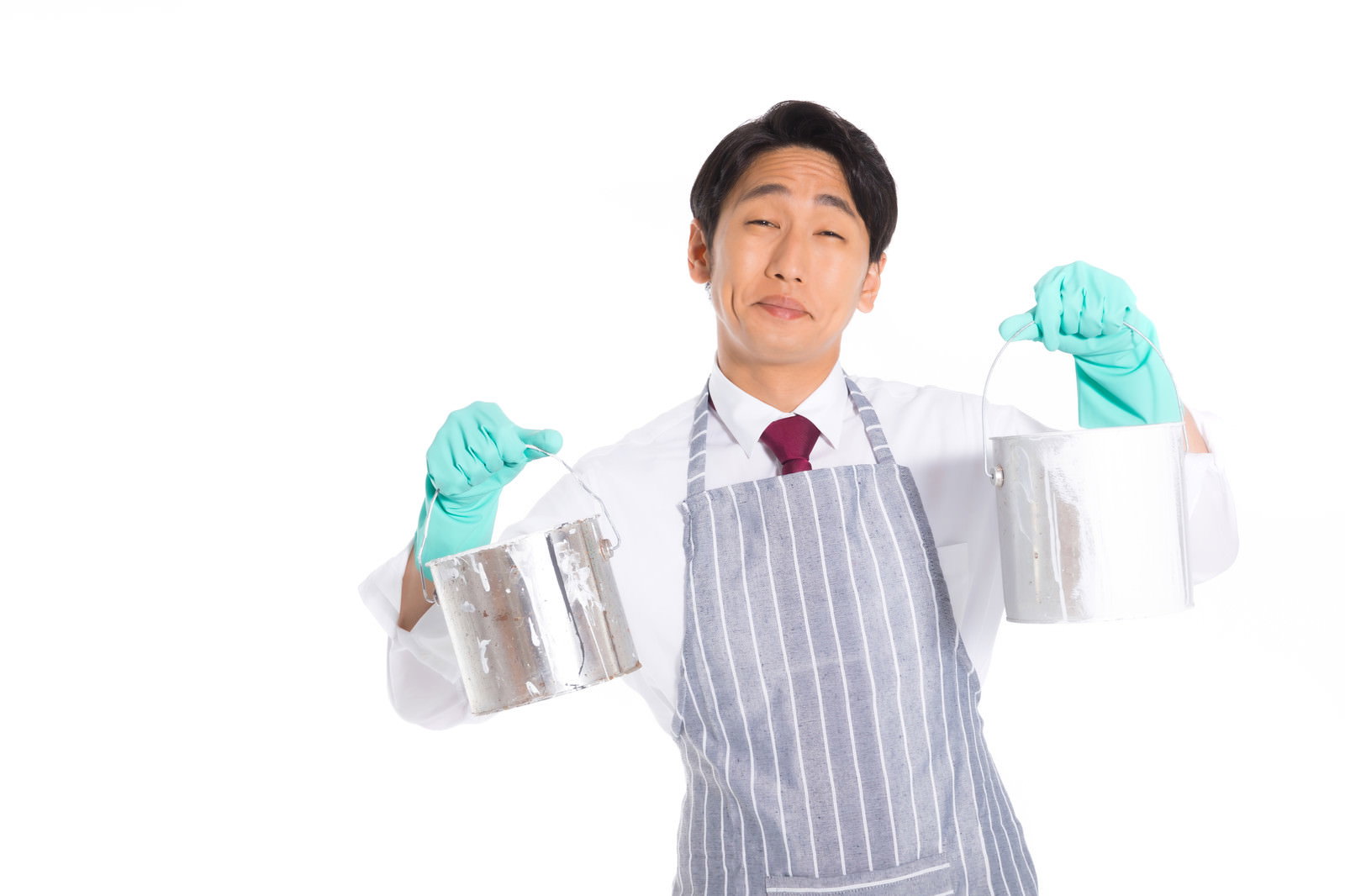 水色のゴム手袋とエプロンを着用してペンキ缶を両手で掲げる営業マン［モデル：大川竜弥］
