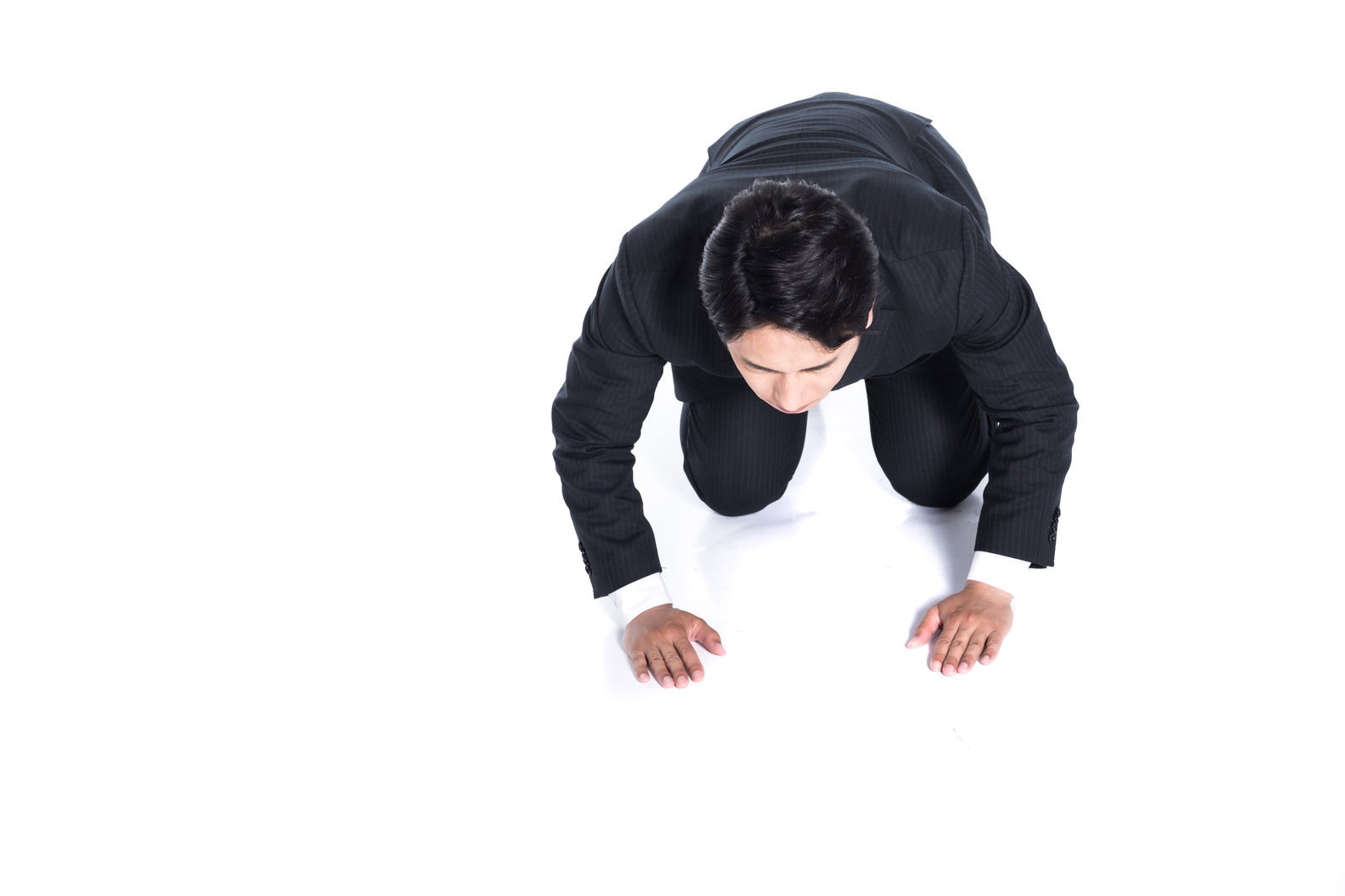 黒いスーツの男性が白い床で両手をついて頭を下げて土下座している俯瞰図［モデル：大川竜弥］