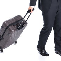 スーツ姿の会社員がトランクをガラガラ引いて歩く出張風景の写真