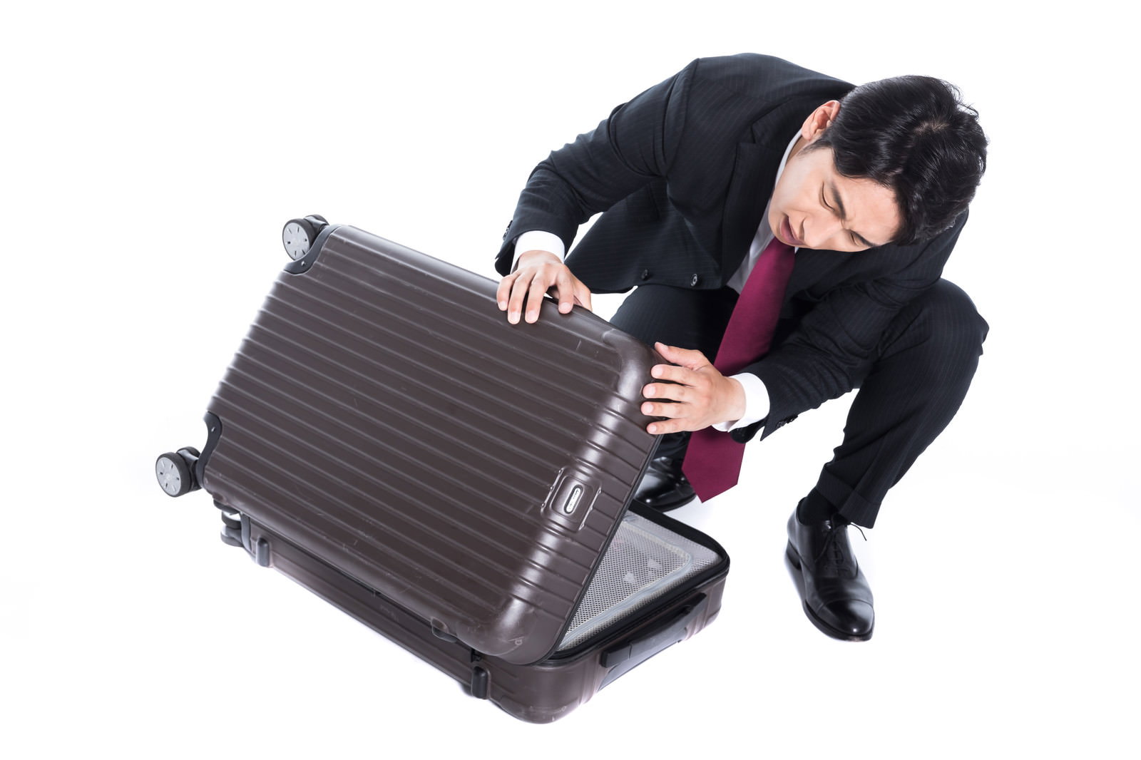 グレーのスーツケースを倒してしまい困った表情の黒いスーツ姿の会社員［モデル：大川竜弥］