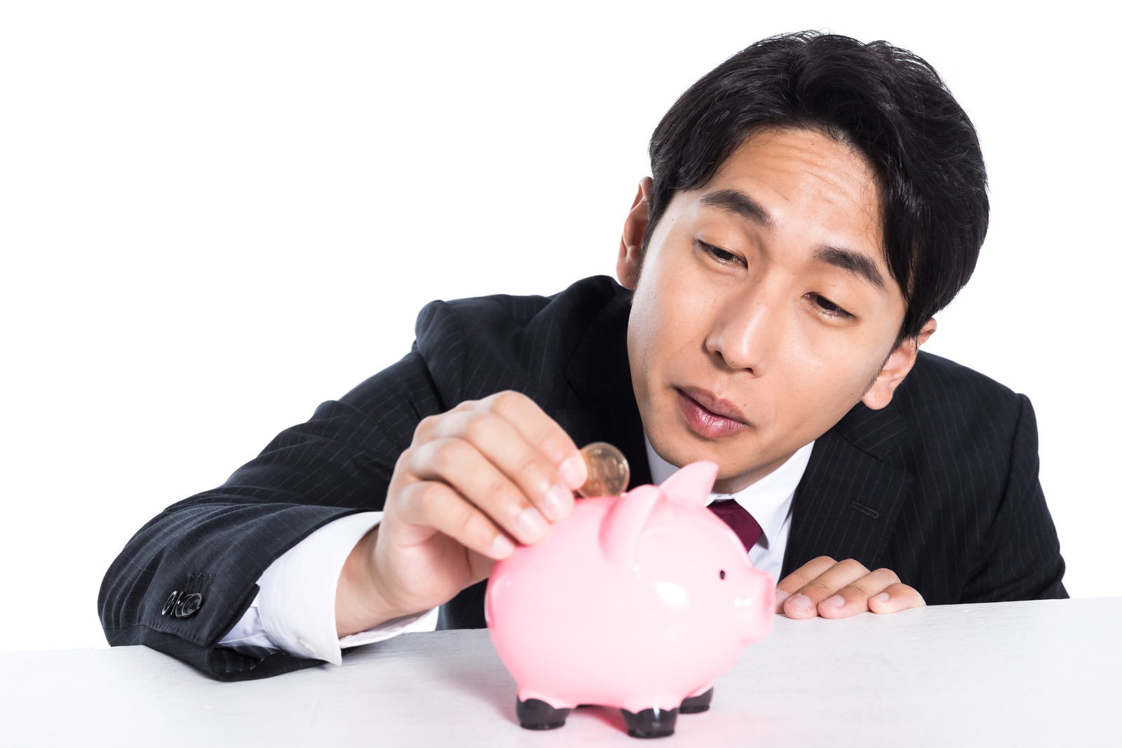 豚の貯金箱に硬貨を入れているスーツ姿の男性［モデル：大川竜弥］