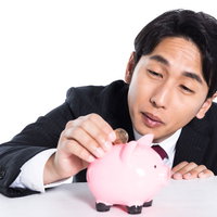 500円玉を貯金箱に入れるスーツ姿の会社員の写真