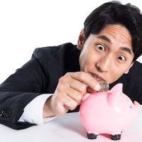 豚の貯金箱になけなしの小銭をいれる会社員の写真