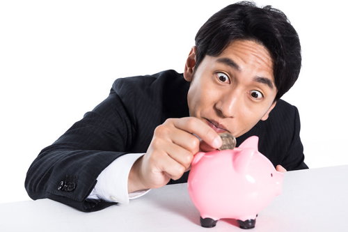 スーツ姿の会社員が豚の貯金箱に小銭を入れる