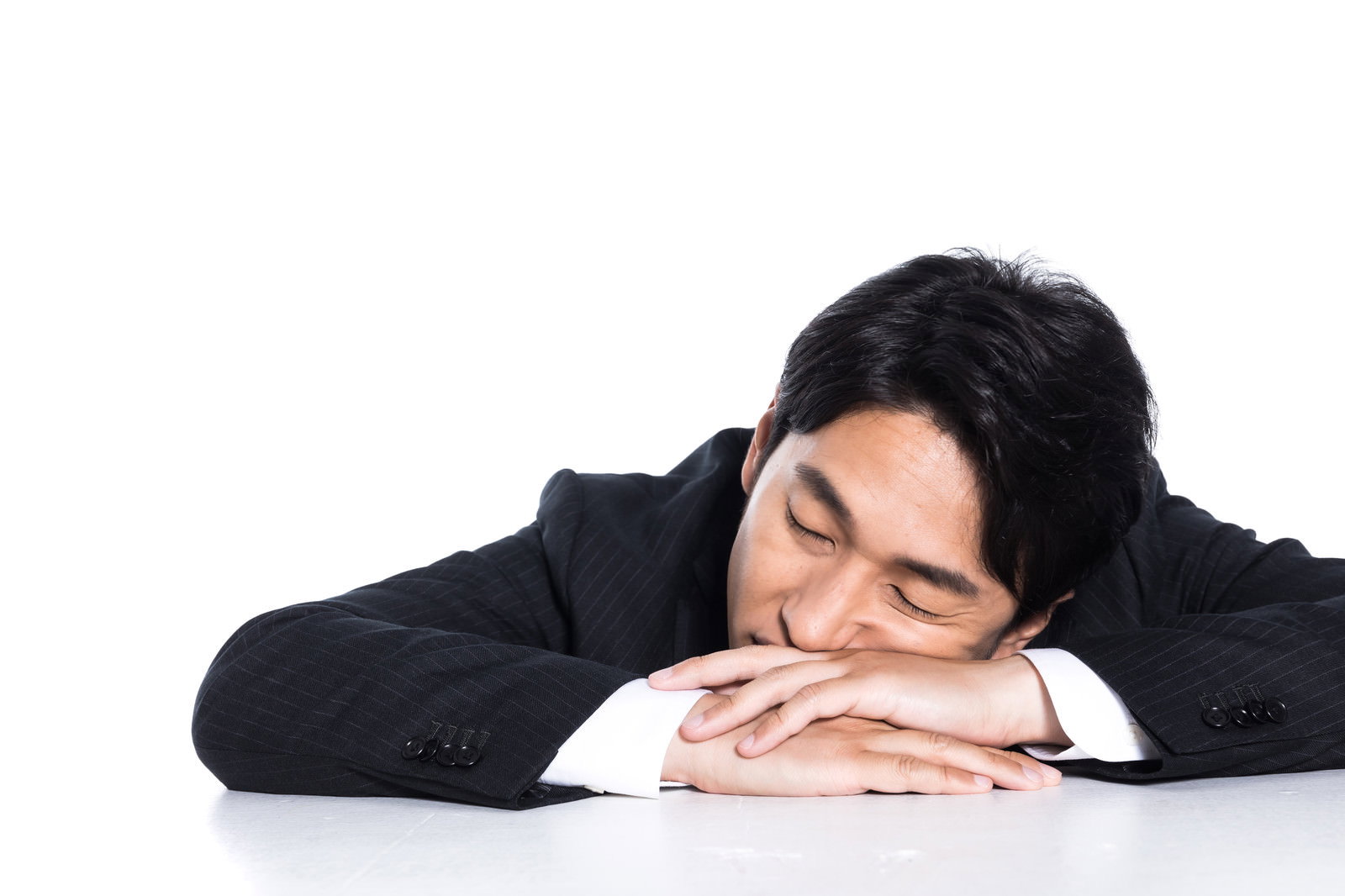 黒いスーツを着た会社員の男性が机にうつぶせになって昼寝している様子［モデル：大川竜弥］